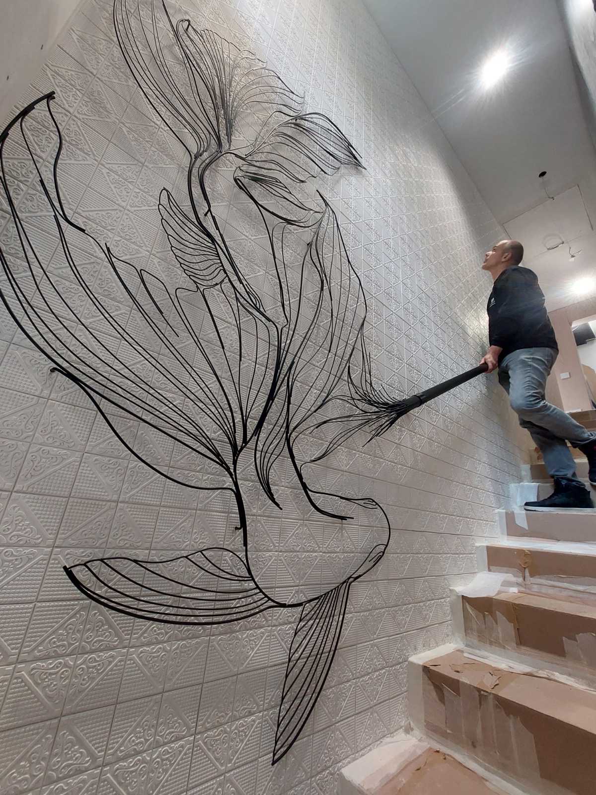 Black wire koi fish sweeping across patterned white tiles beside the staircase, with the craftsman fitting the handrail