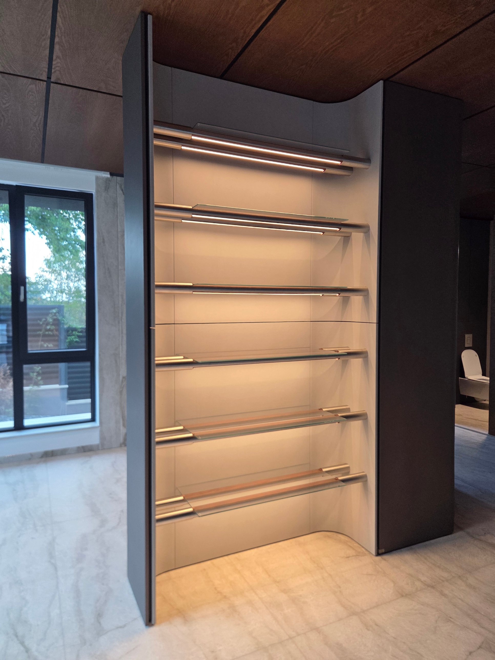 A curved storage niche with lit stainless rails and glass shelves within a dark frame