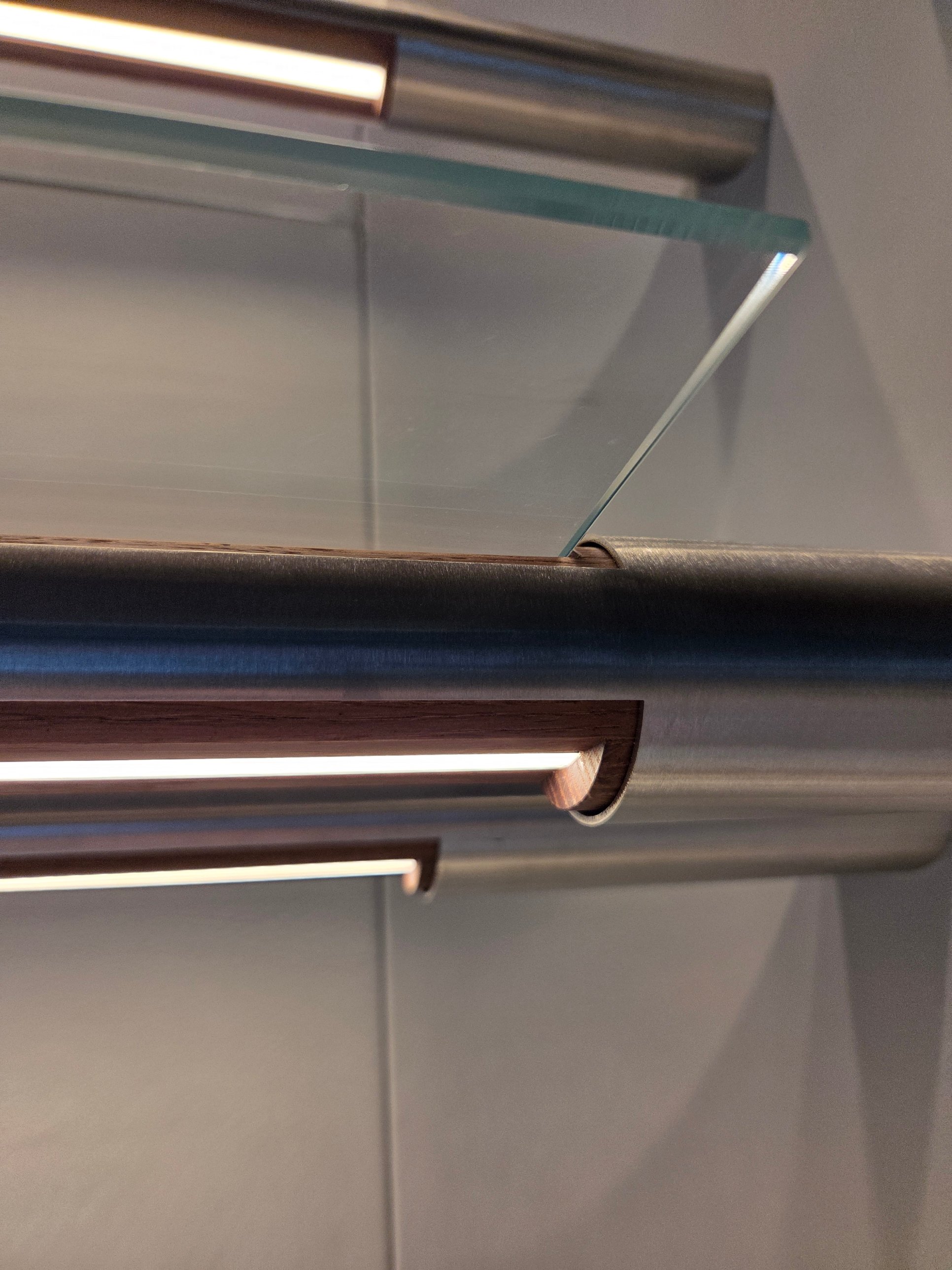 A glass shelf resting in a stainless rail with a timber insert and a line of light