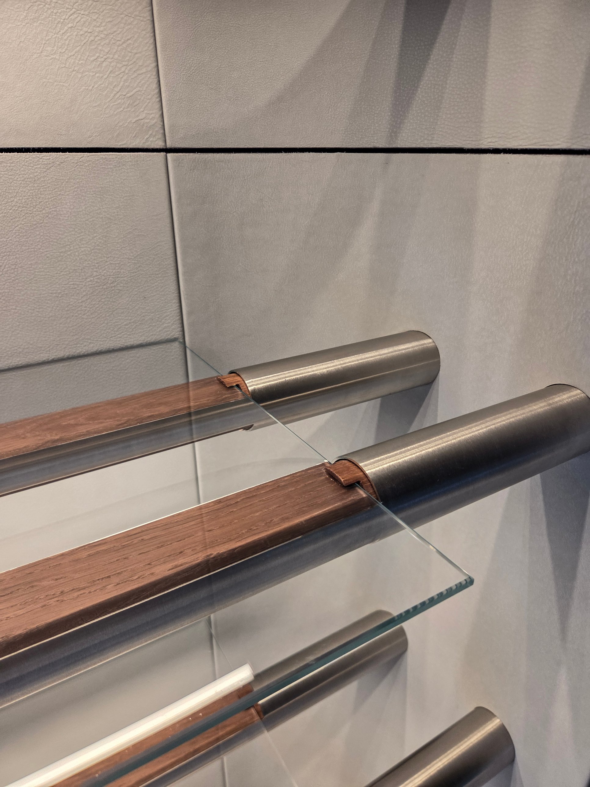 Stainless rails with timber inserts holding glass shelves against a leather wall