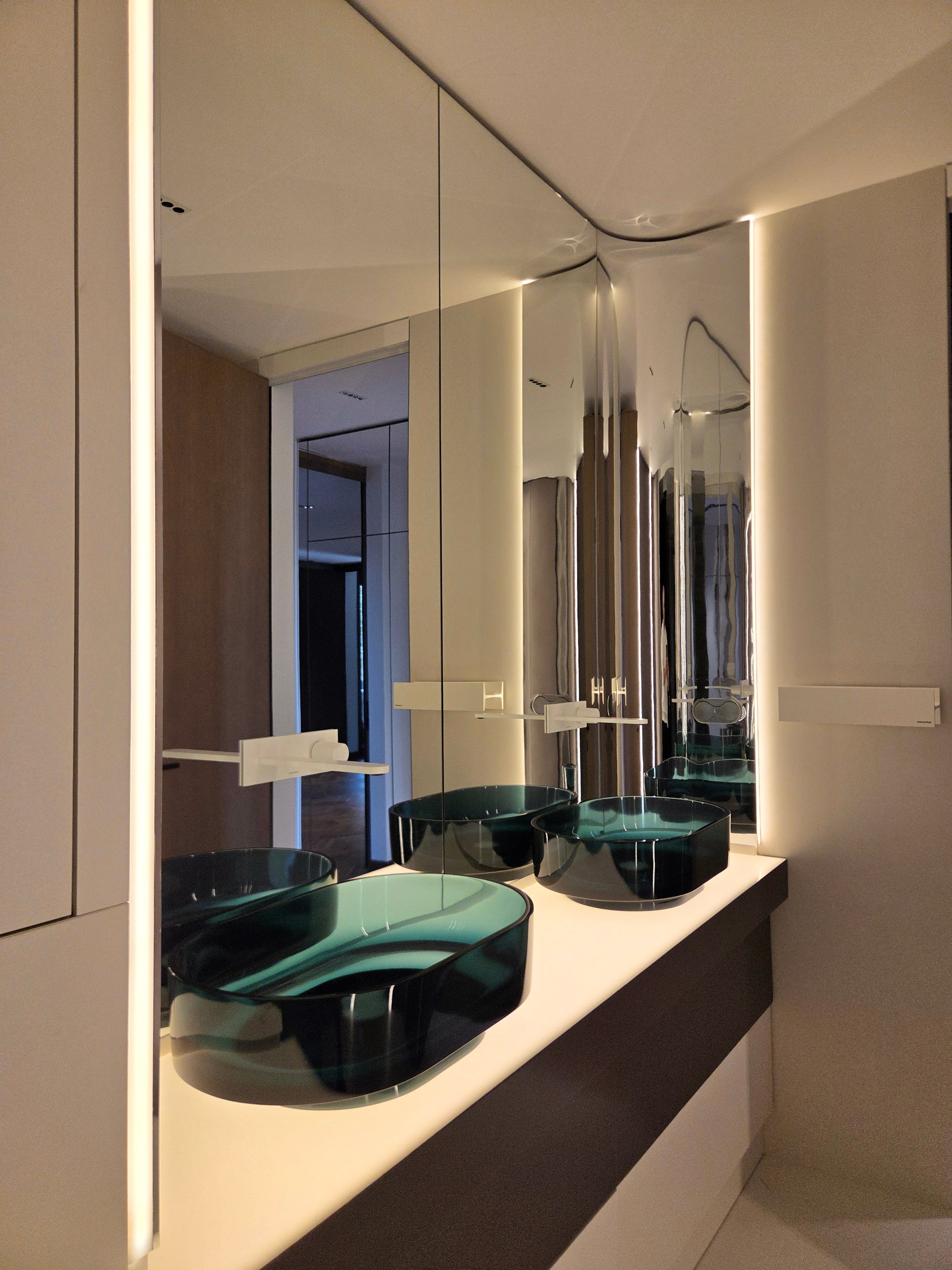 Translucent teal basins on a pale counter before a lit mirror