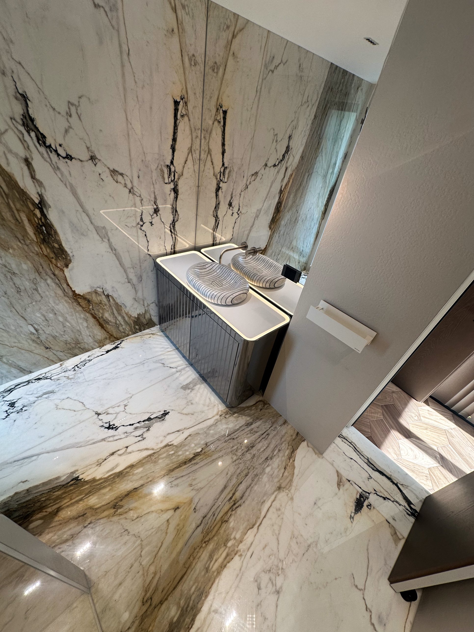 A striped vessel basin on a glowing vanity within pale veined stone