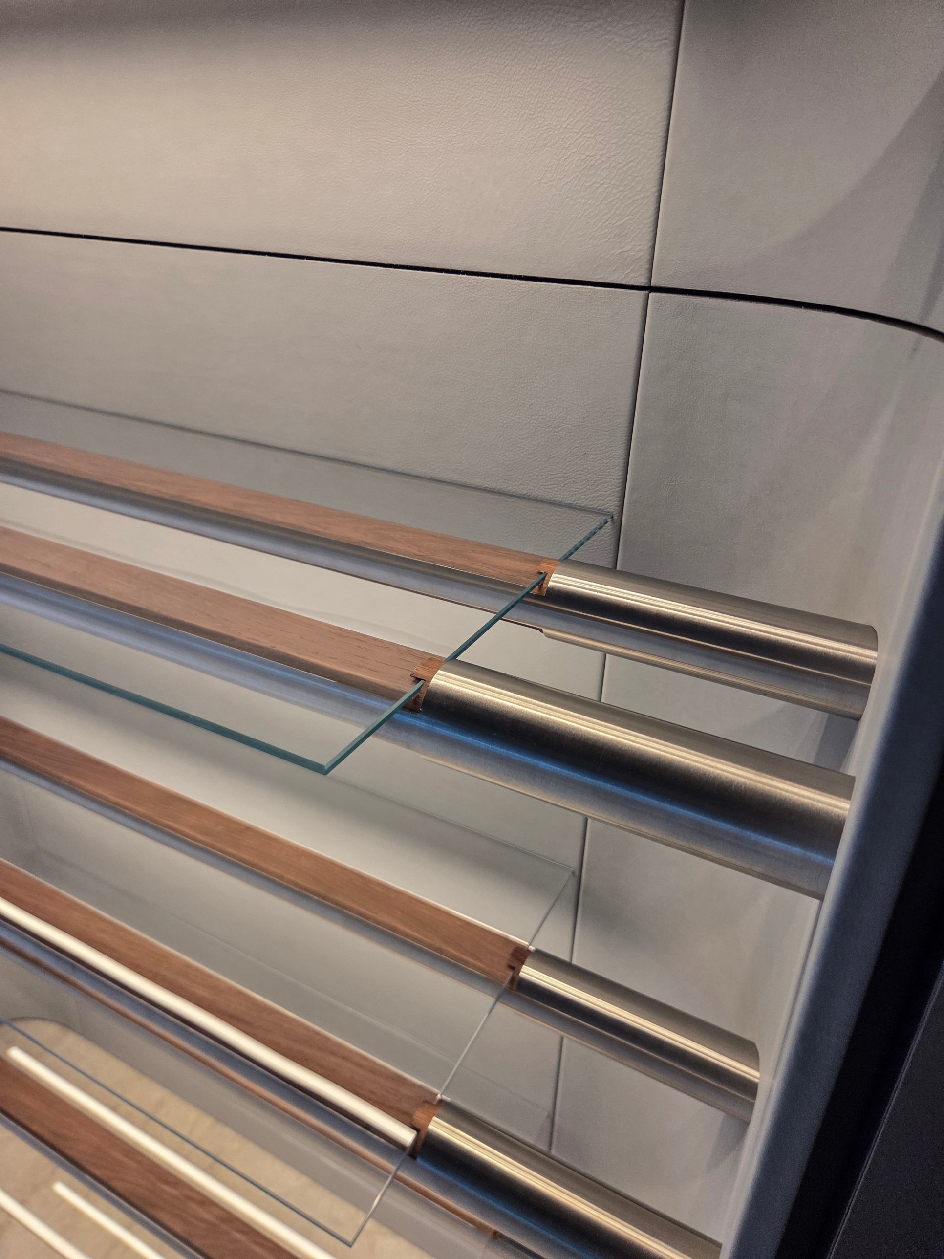Glass shelves on stainless rails against the leather wall