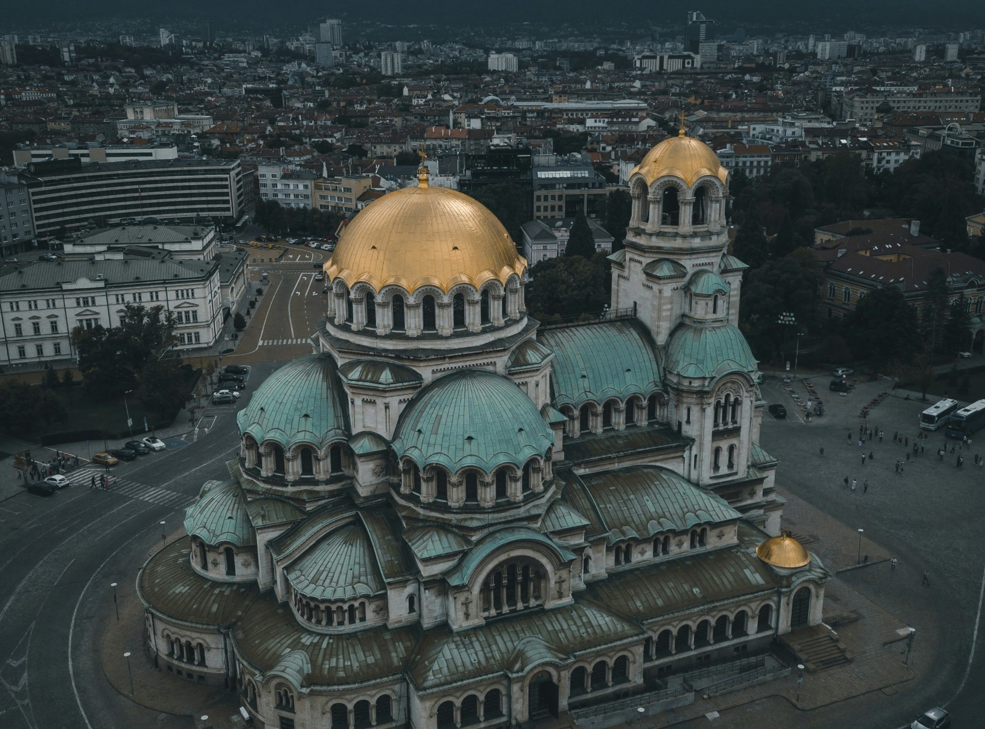 The golden domes of the Alexander Nevsky Cathedral seen from above, with Vitosha mountain beneath a stormy sky