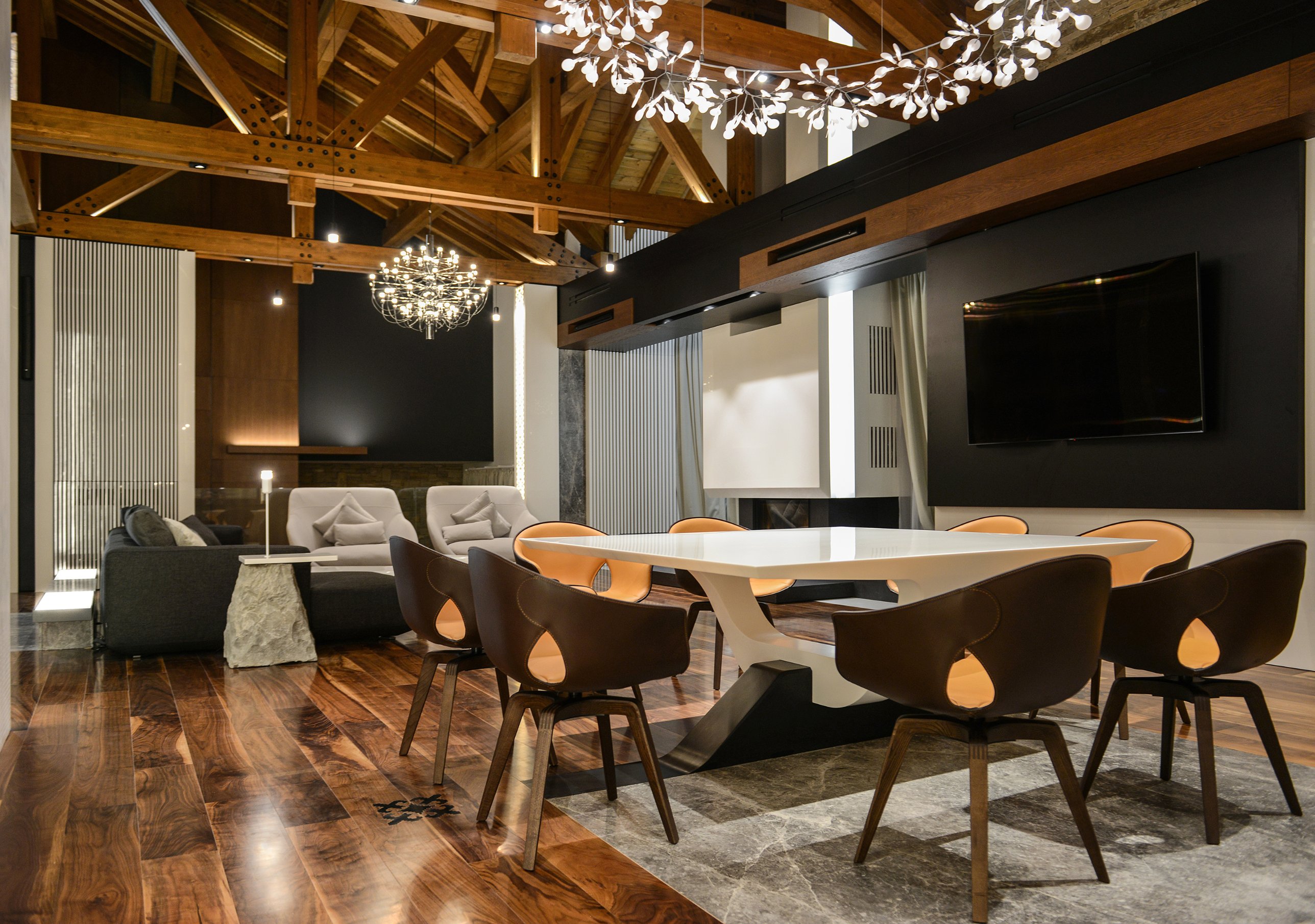 Open dining and living area beneath the timber roof, with branching chandeliers and leather chairs