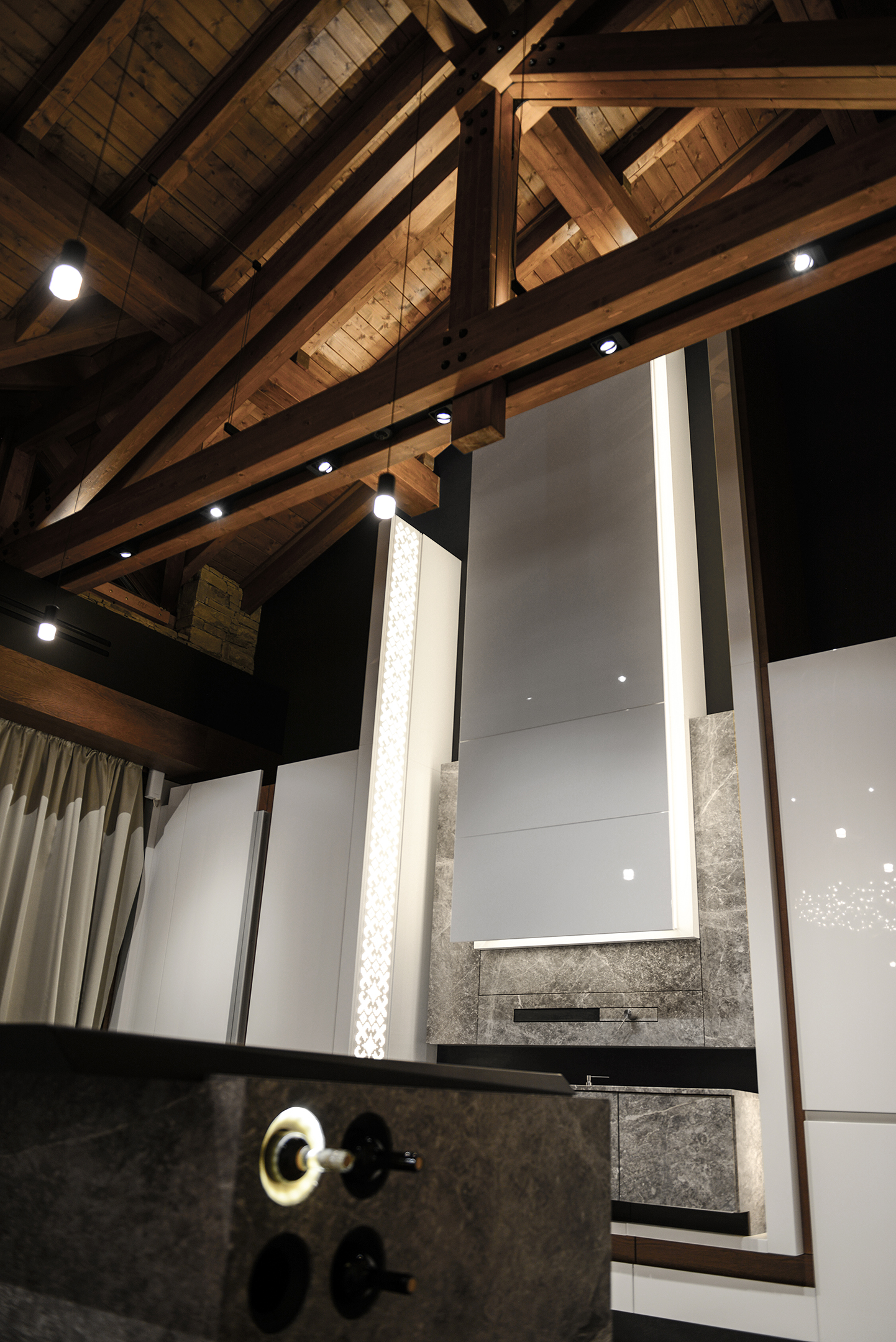 Exposed timber trusses above the tall kitchen wall and its illuminated pattern panel
