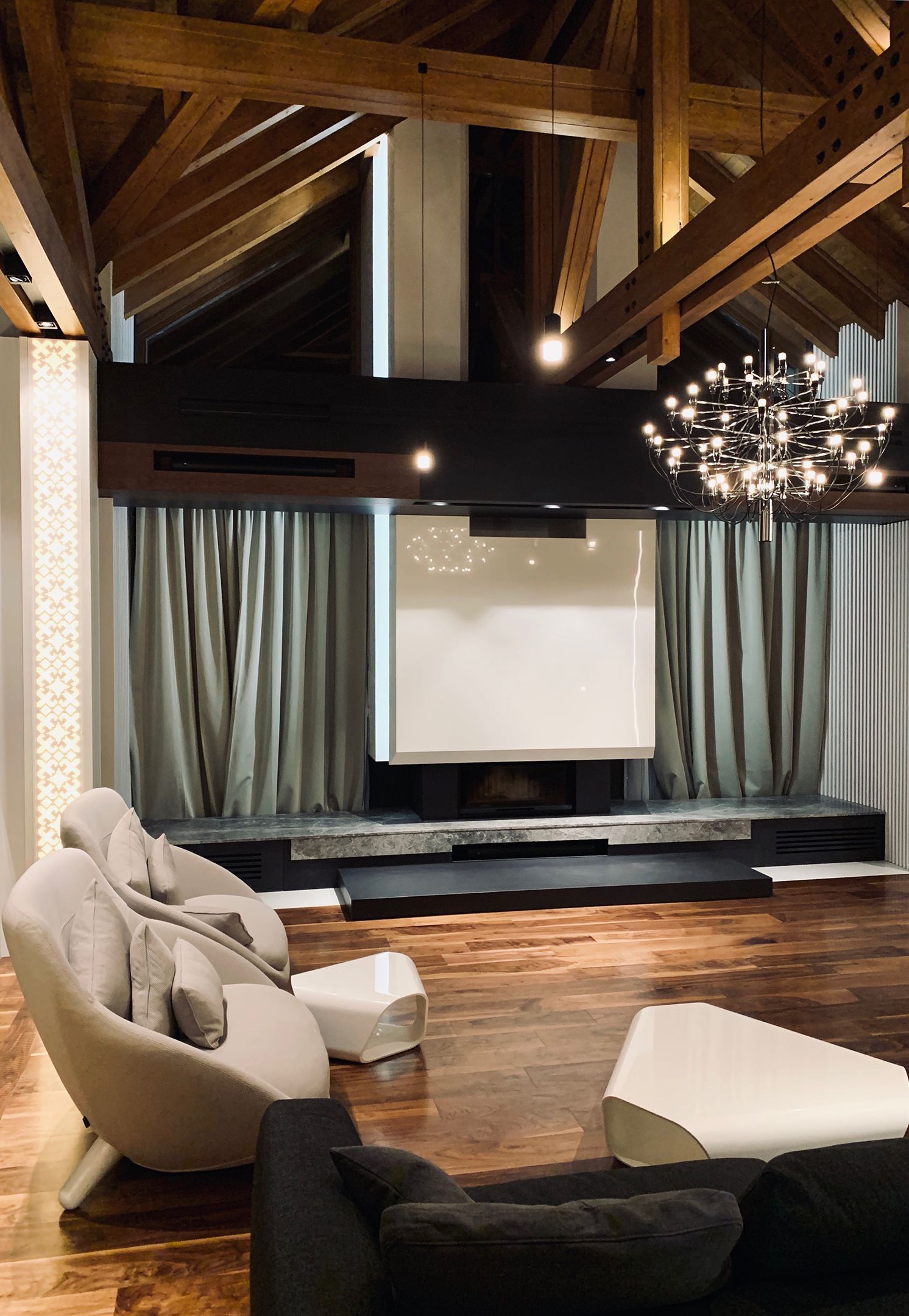 Living area with pale armchairs and full-height curtains beneath the timber roof