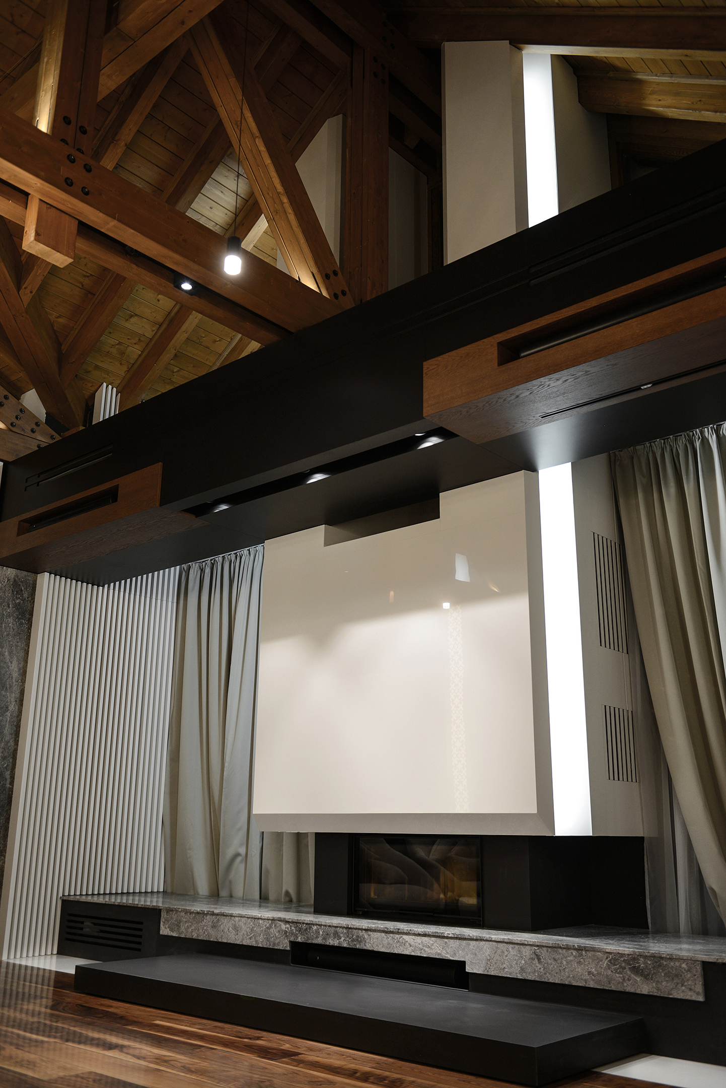 The fireplace wall rising toward the timber roof, framed by a line of light