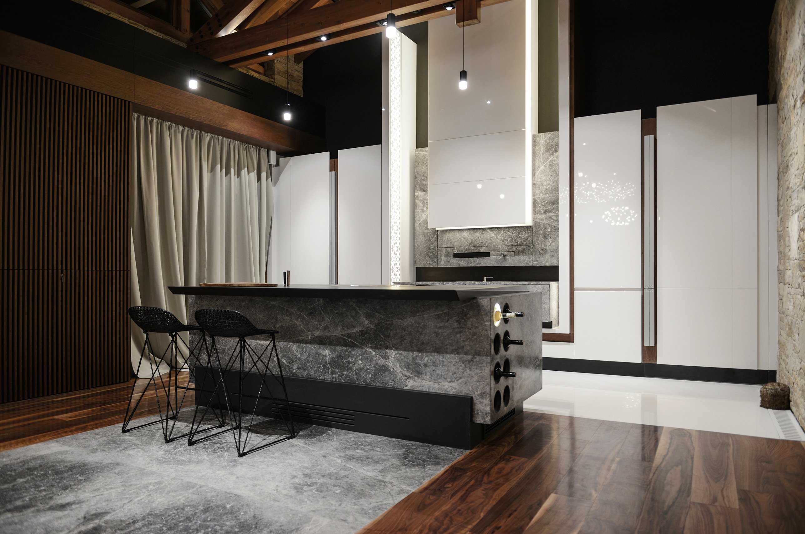 The kitchen: a stone island with bar stools before tall white cabinetry