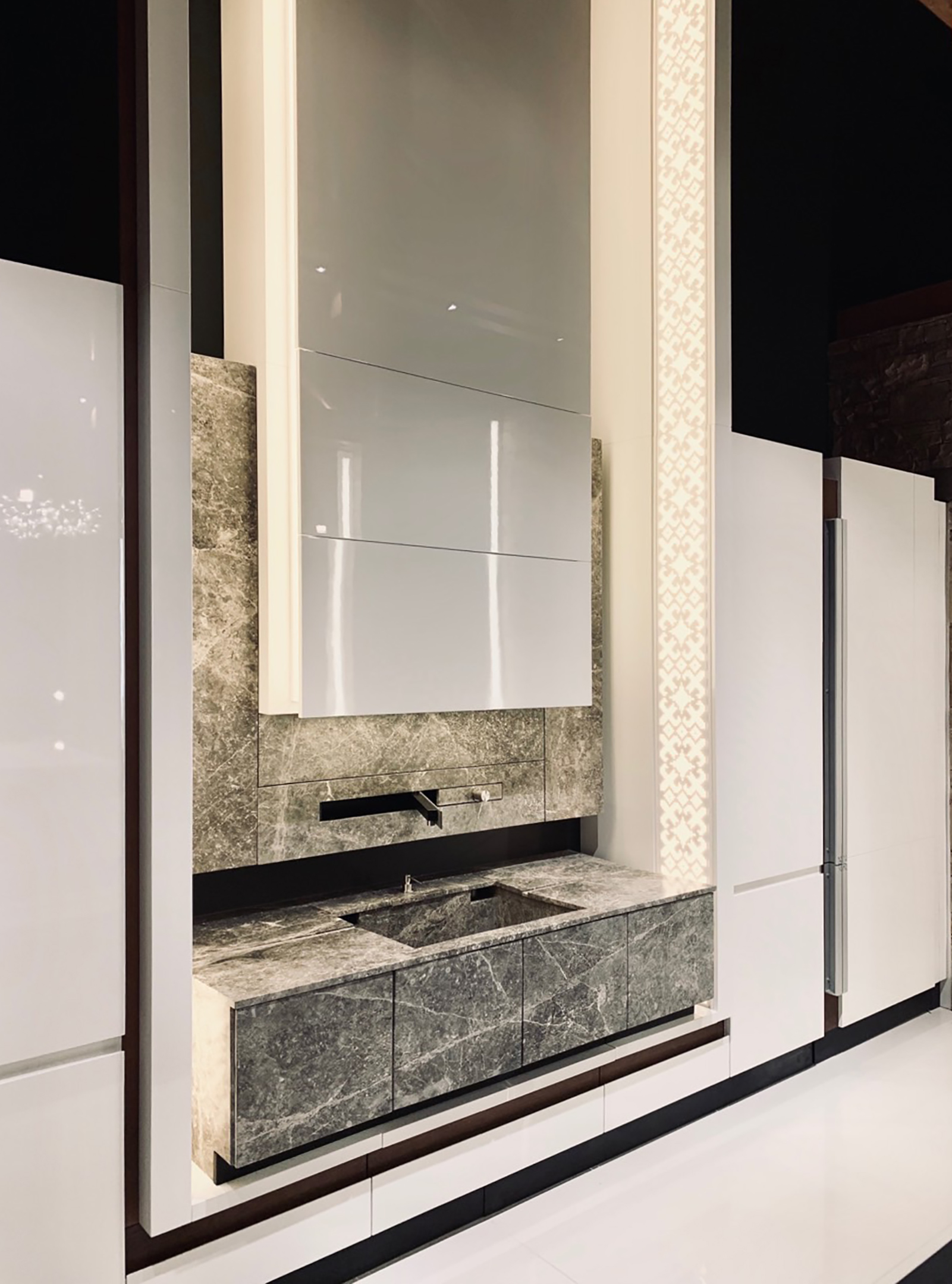 The stone kitchen wall framed by white gloss cabinetry and an illuminated pattern