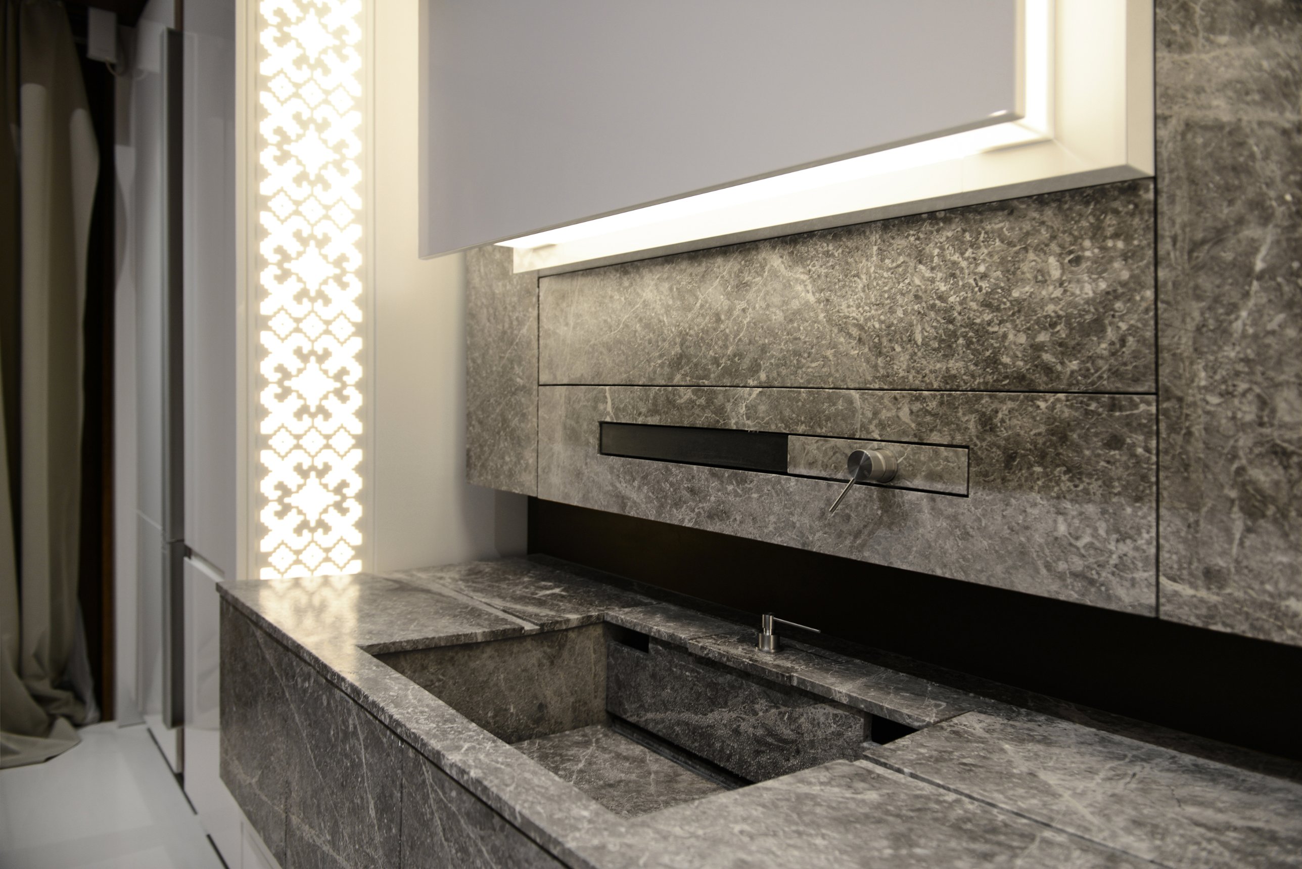 The stone sink set into the worktop beneath a lit panel and a slot-mounted tap