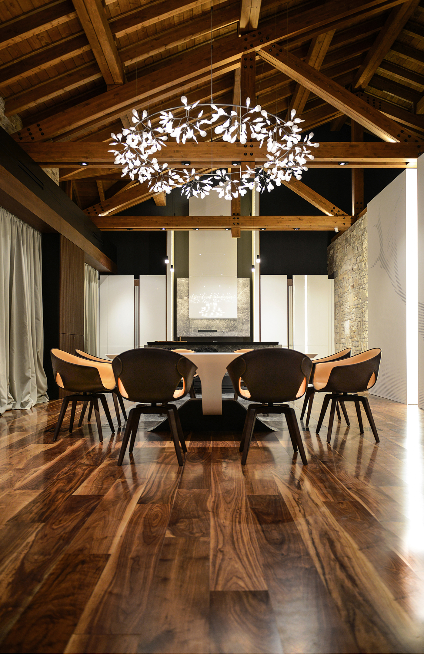 The dining table beneath a luminous branching chandelier and the timber roof