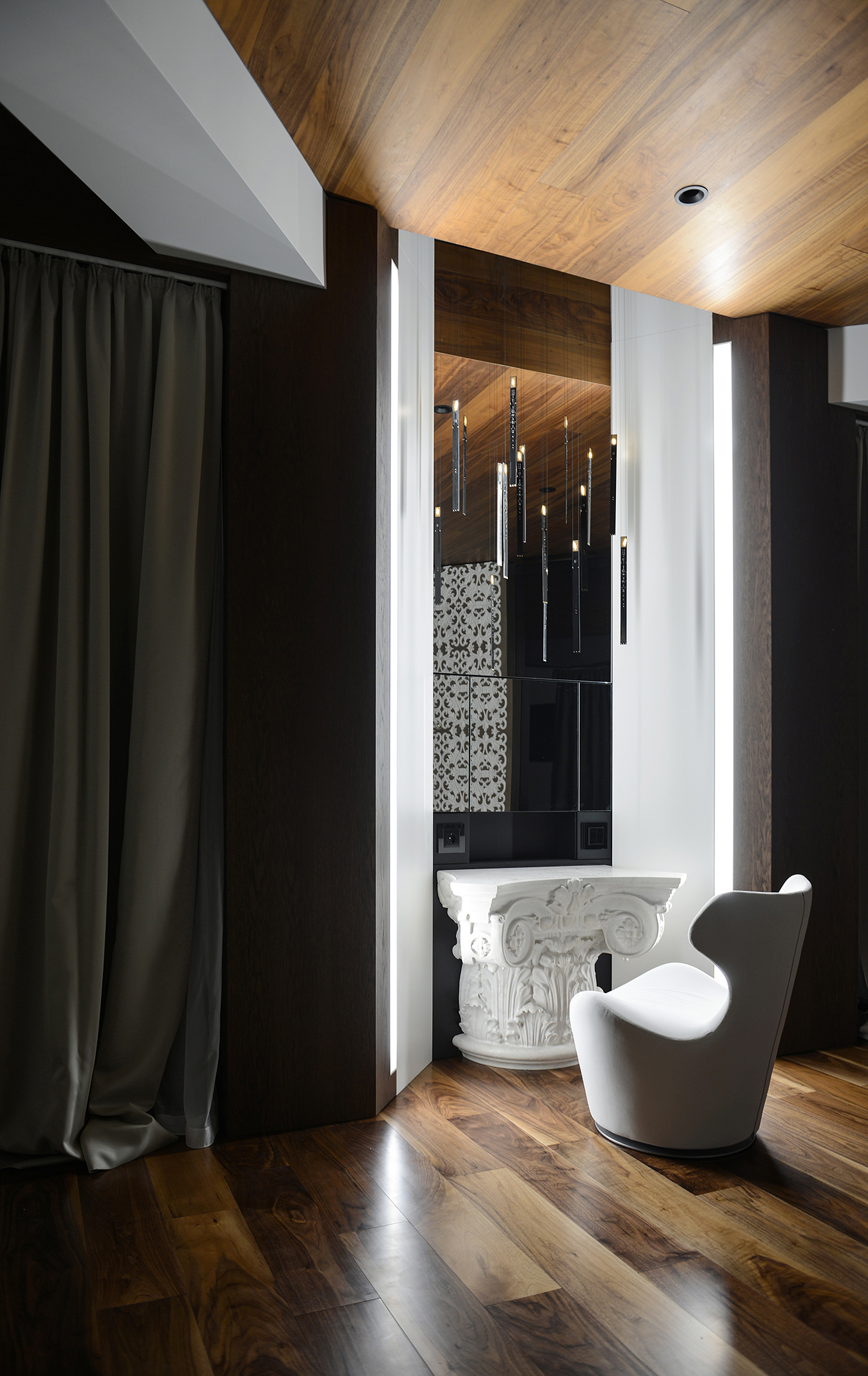 A classical stone capital used as a console beneath pendant lights and a walnut ceiling