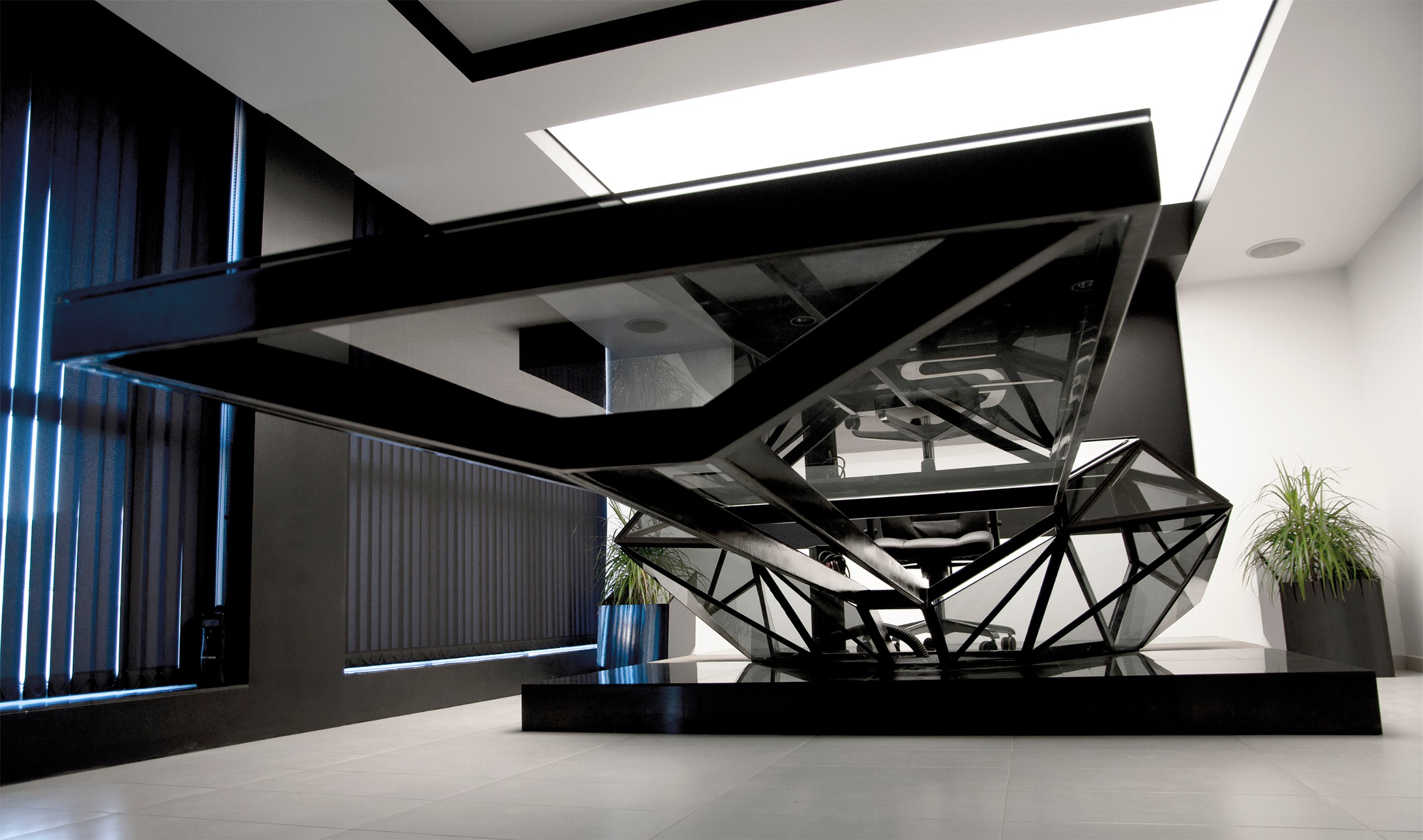 The desk seen from below, its cantilevered frame rising toward the illuminated ceiling