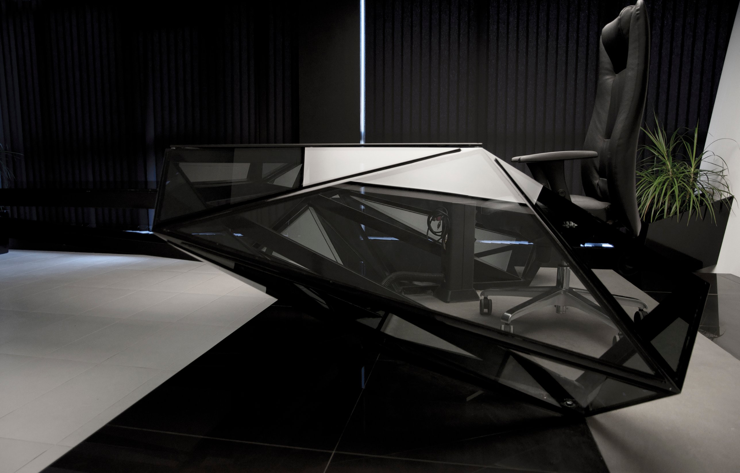 The faceted glass desk in profile before dark vertical blinds