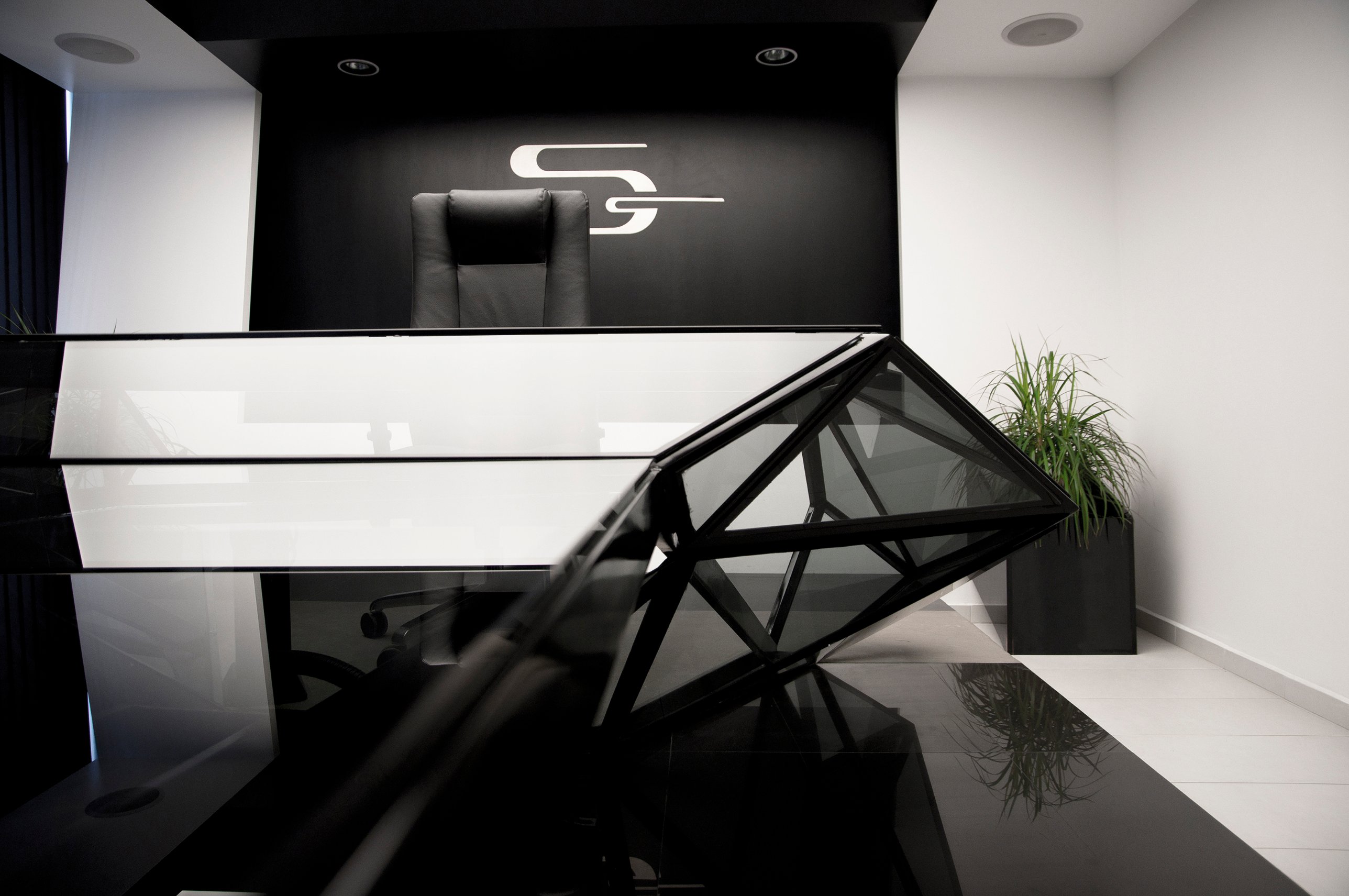 The faceted glass prow of the desk reaching toward the executive chair and emblem