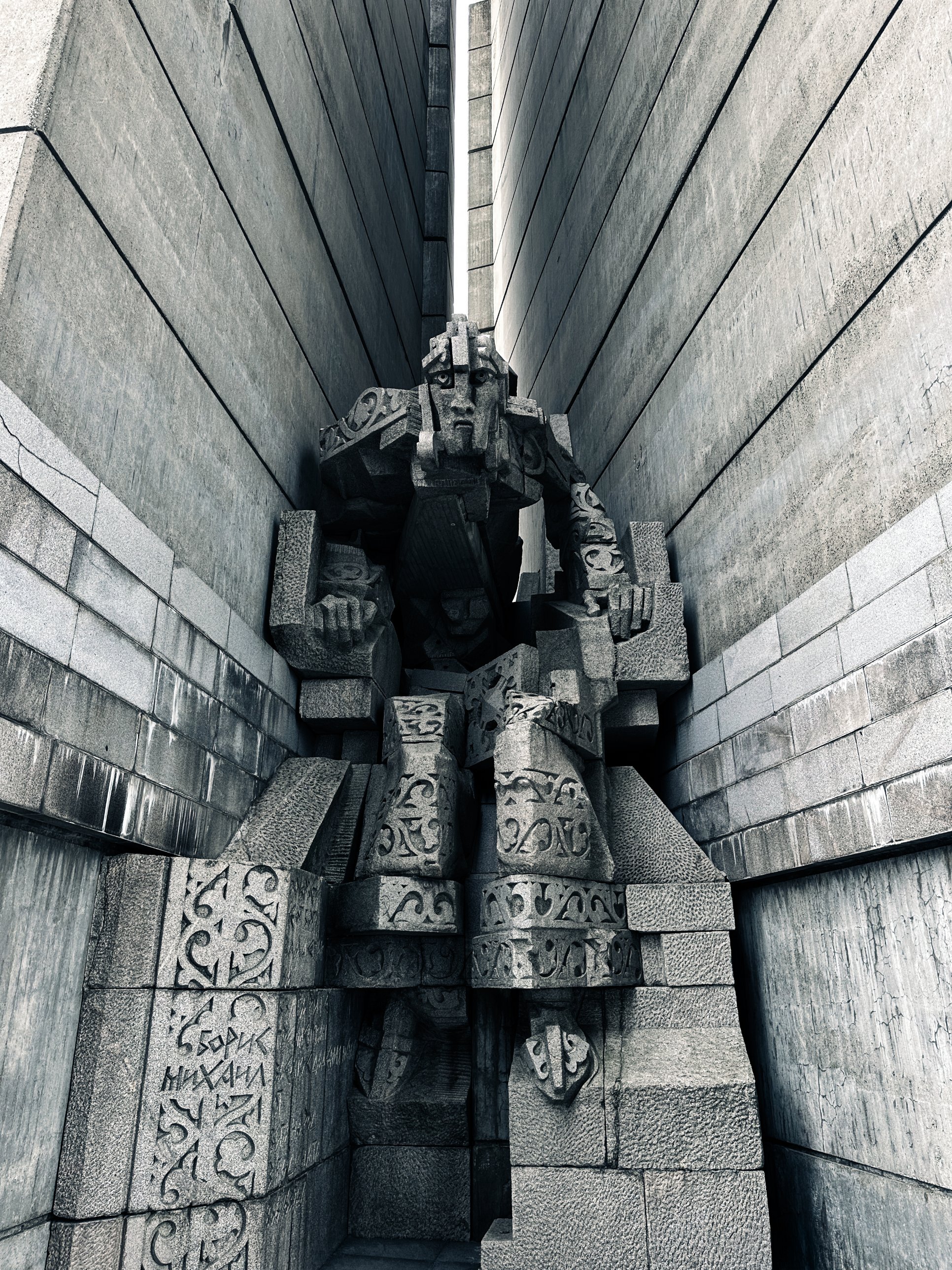 A seated stone figure framed between the concrete walls of the Shumen monument