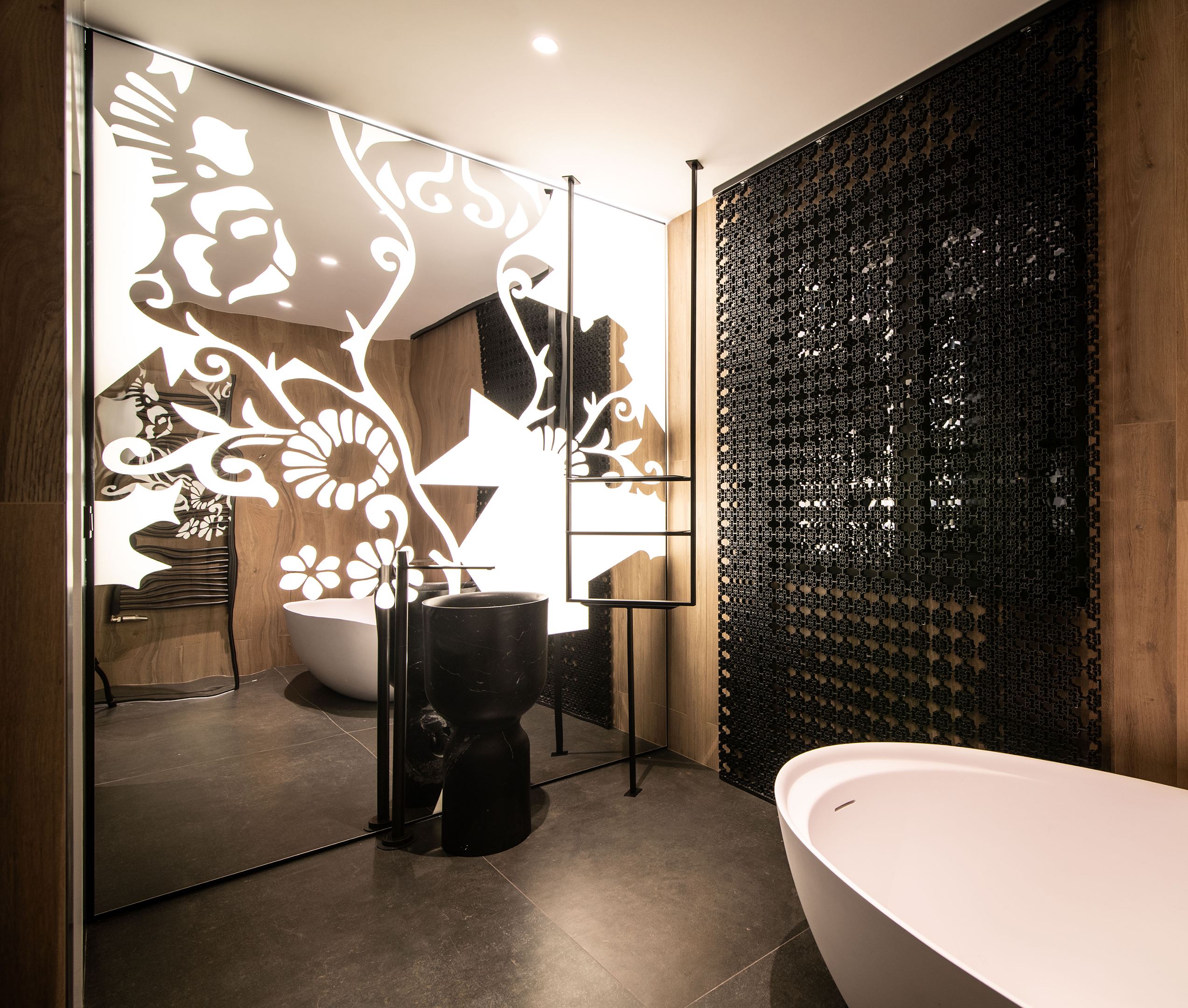Bathroom with a black basin before an illuminated floral mirror wall and a perforated screen