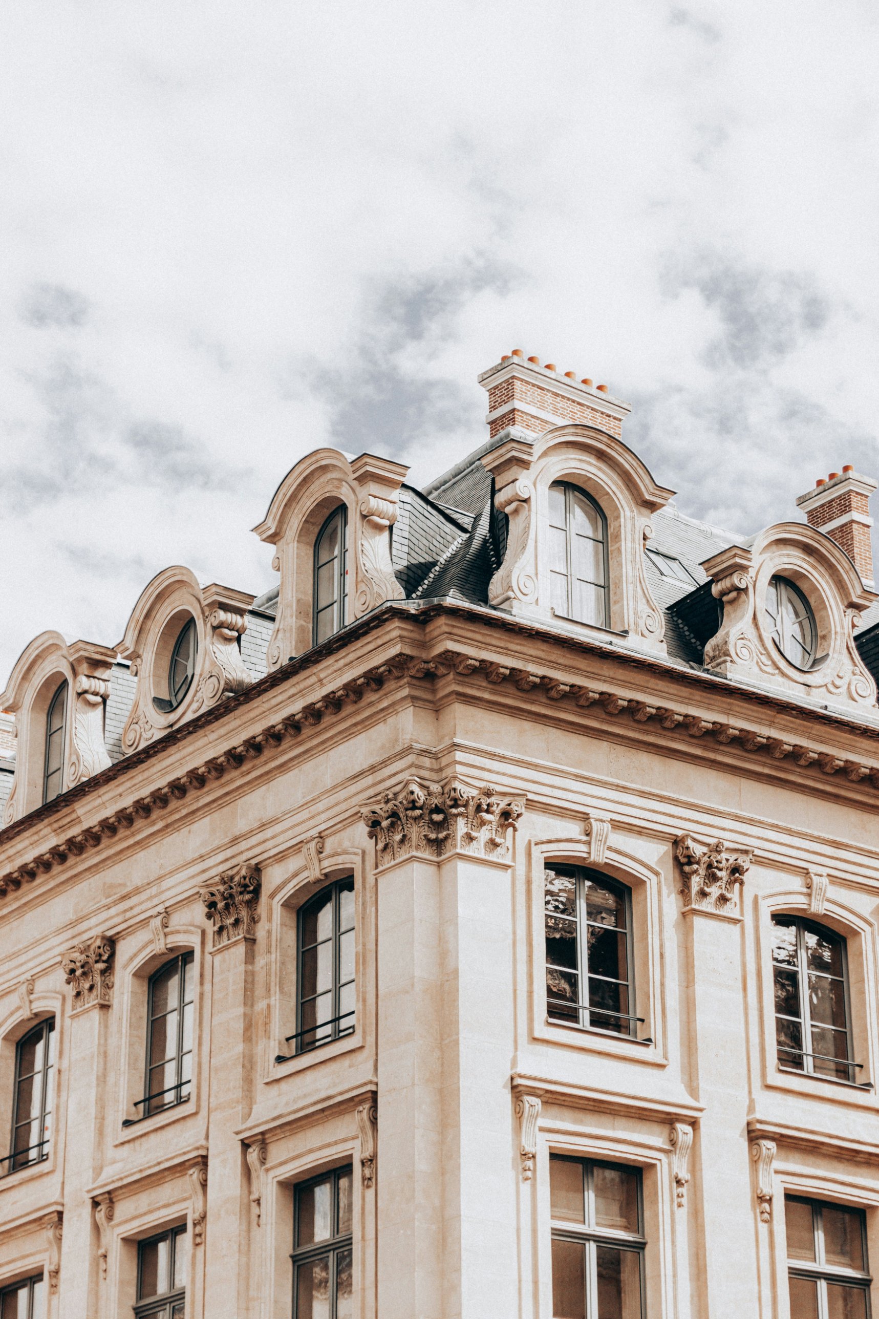 A Parisian stone facade with carved dormer windows beneath a cloudy sky